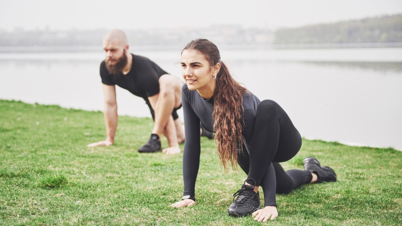fitness-couple-stretching-outdoors-park-near-water-young-bearded-man-woman-exercising-together-morning_146671-14796