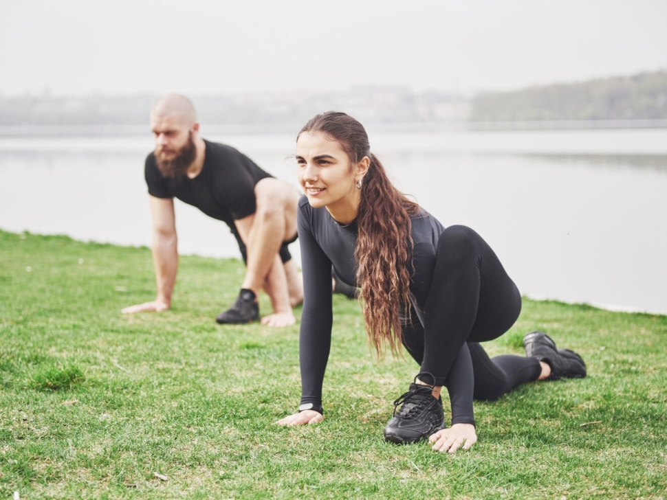 fitness-couple-stretching-outdoors-park-near-water-young-bearded-man-woman-exercising-together-morning_146671-14796